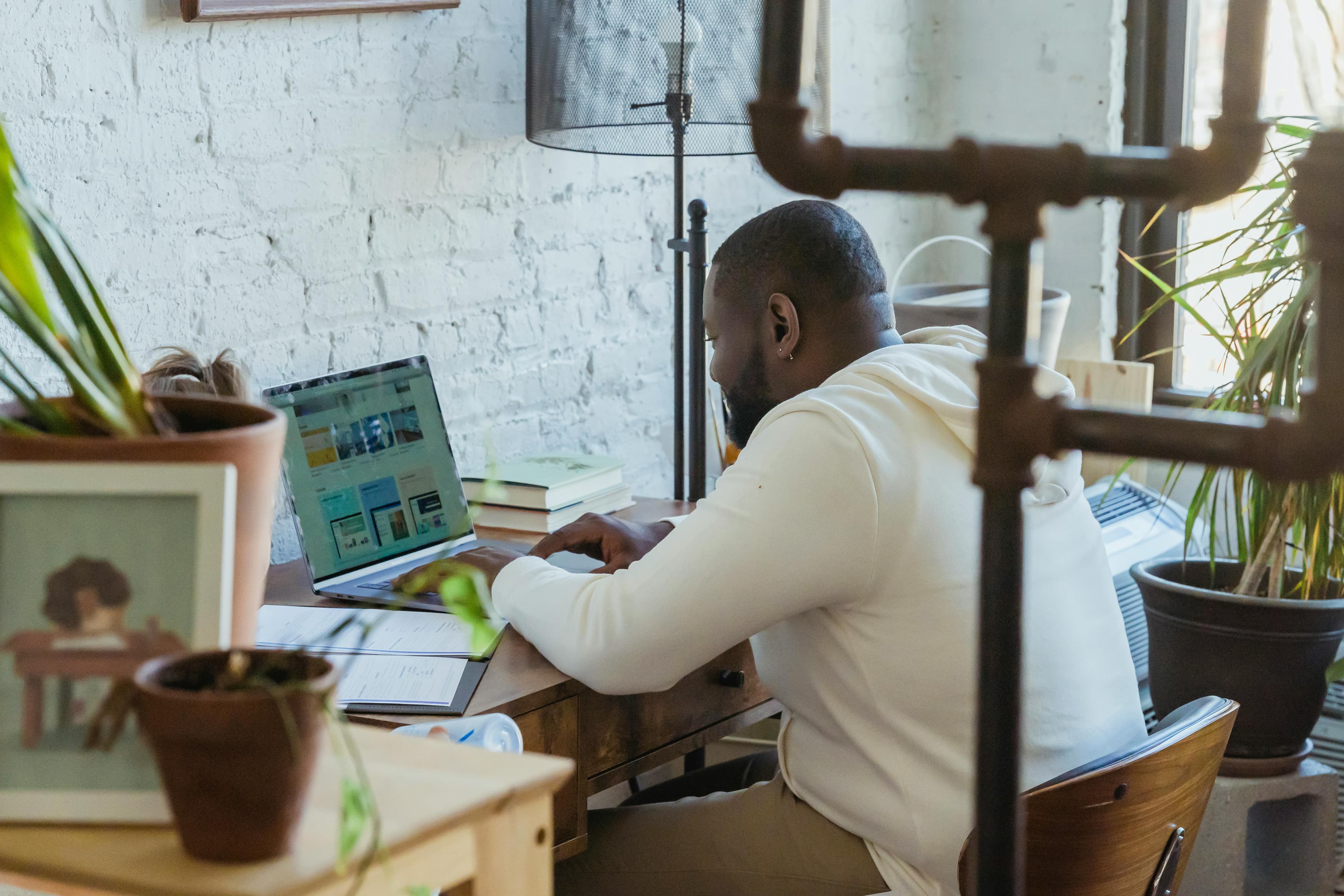 A man working intently on his laptop in a cozy, plant-filled workspace. This image can be used to illustrate the "manager vs leader" concept, highlighting the focused, task-oriented nature of a manager.