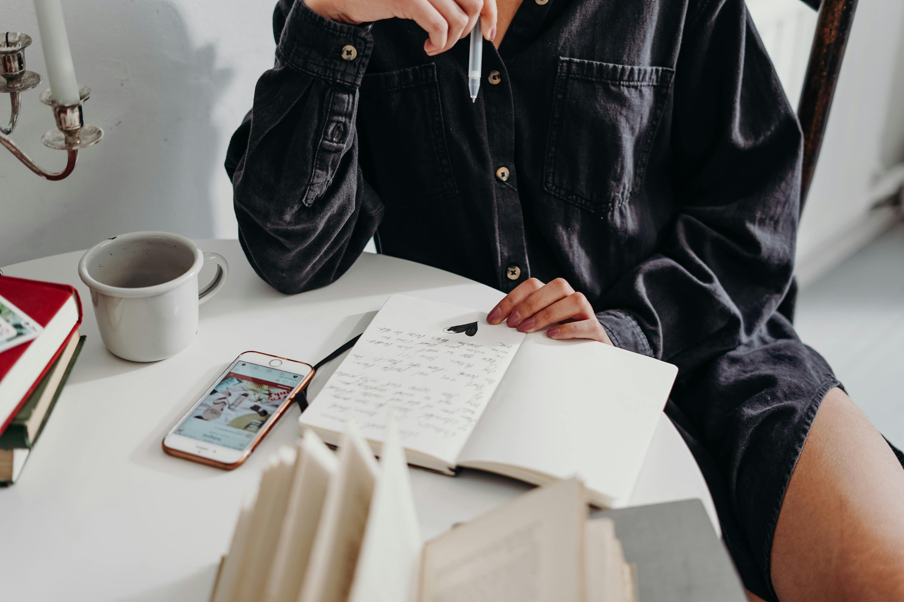 A person thoughtfully writing notes in a journal, accompanied by a smartphone, symbolizing content creation strategies for "adaptive SEO solutions."