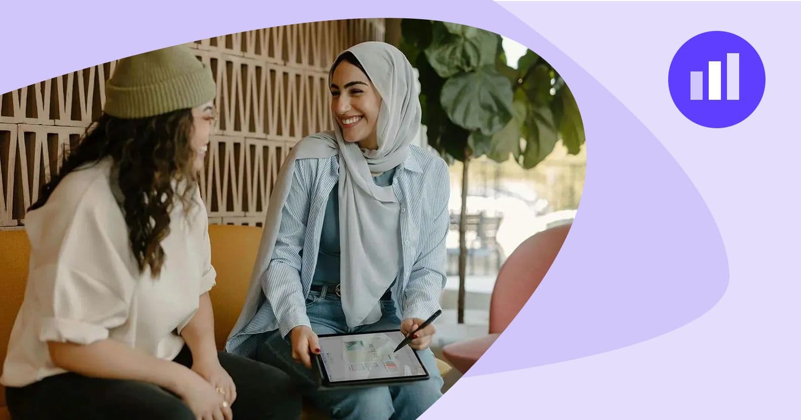 Two women, one wearing a hijab, sharing ideas and reviewing a tablet in a casual yet professional setting. This image captures the collaborative and customer-centric strategies that define a B2B SaaS marketing agency's approach to building relationships and solutions.