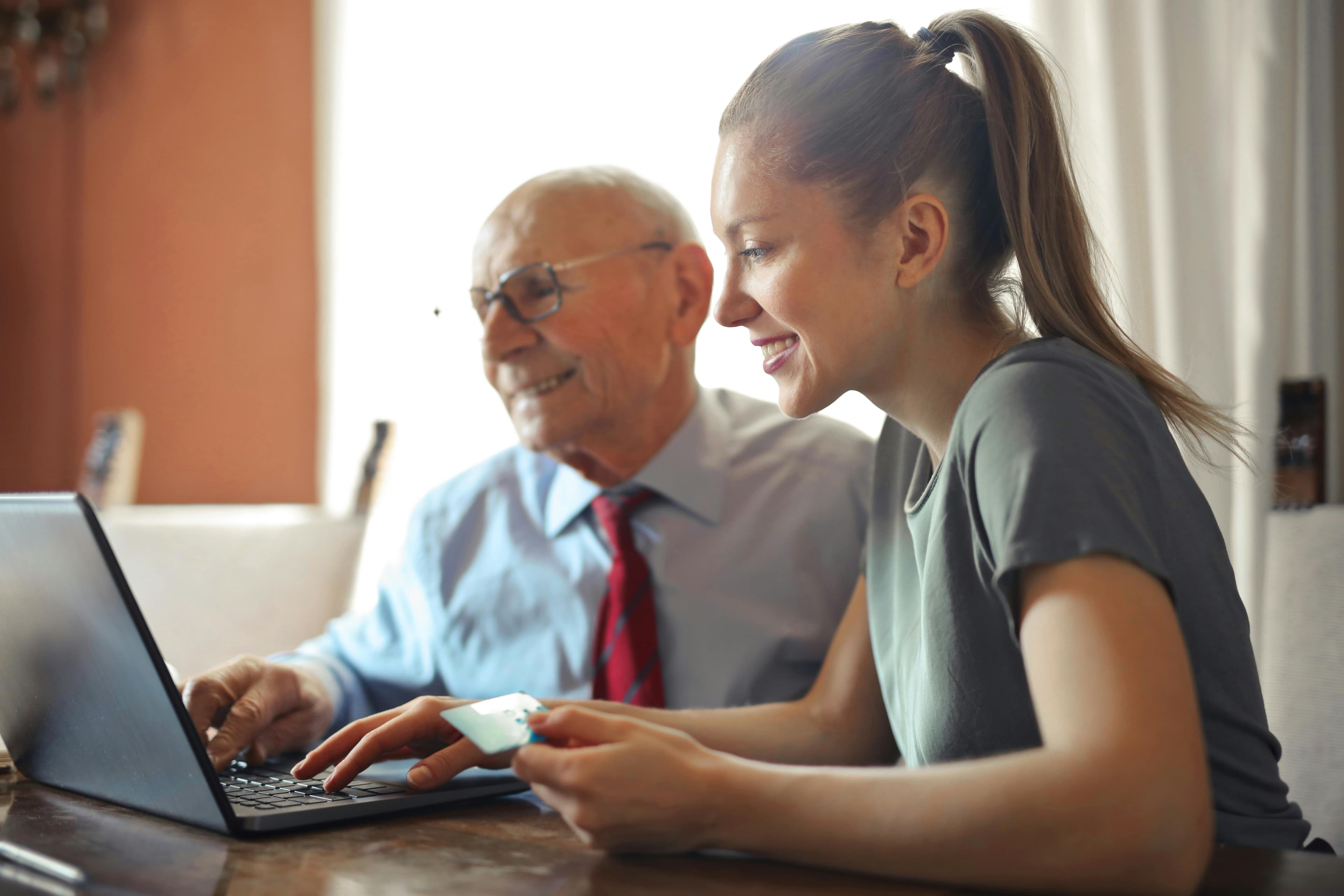 A young woman assisting an elderly man with online navigation on a laptop, showing the inclusivity and reach of search engine marketing in guiding all age groups.