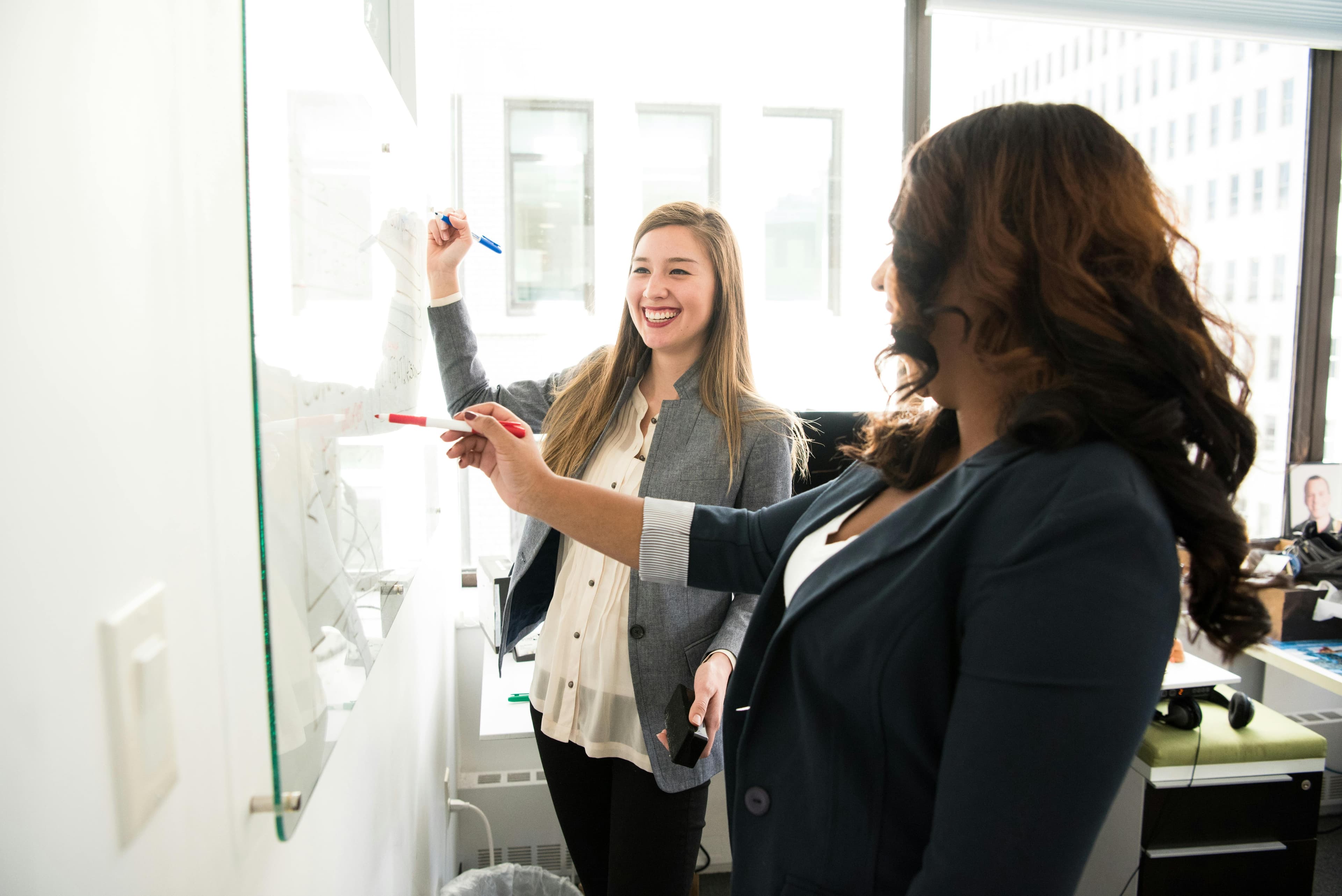 Two colleagues enthusiastically brainstorming at a whiteboard, highlighting collaboration in "AI and creative writing."