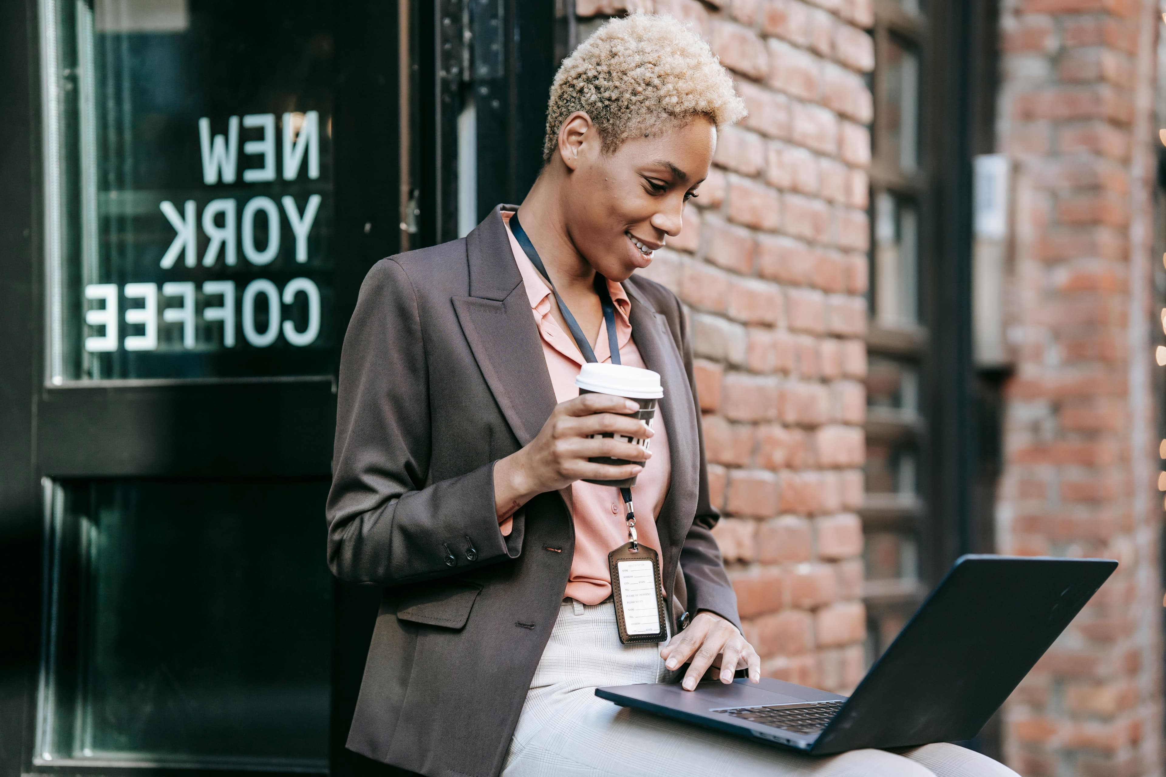 Professional woman holding a coffee cup and using a laptop outdoors, representing on-the-go search engine optimization opportunities.