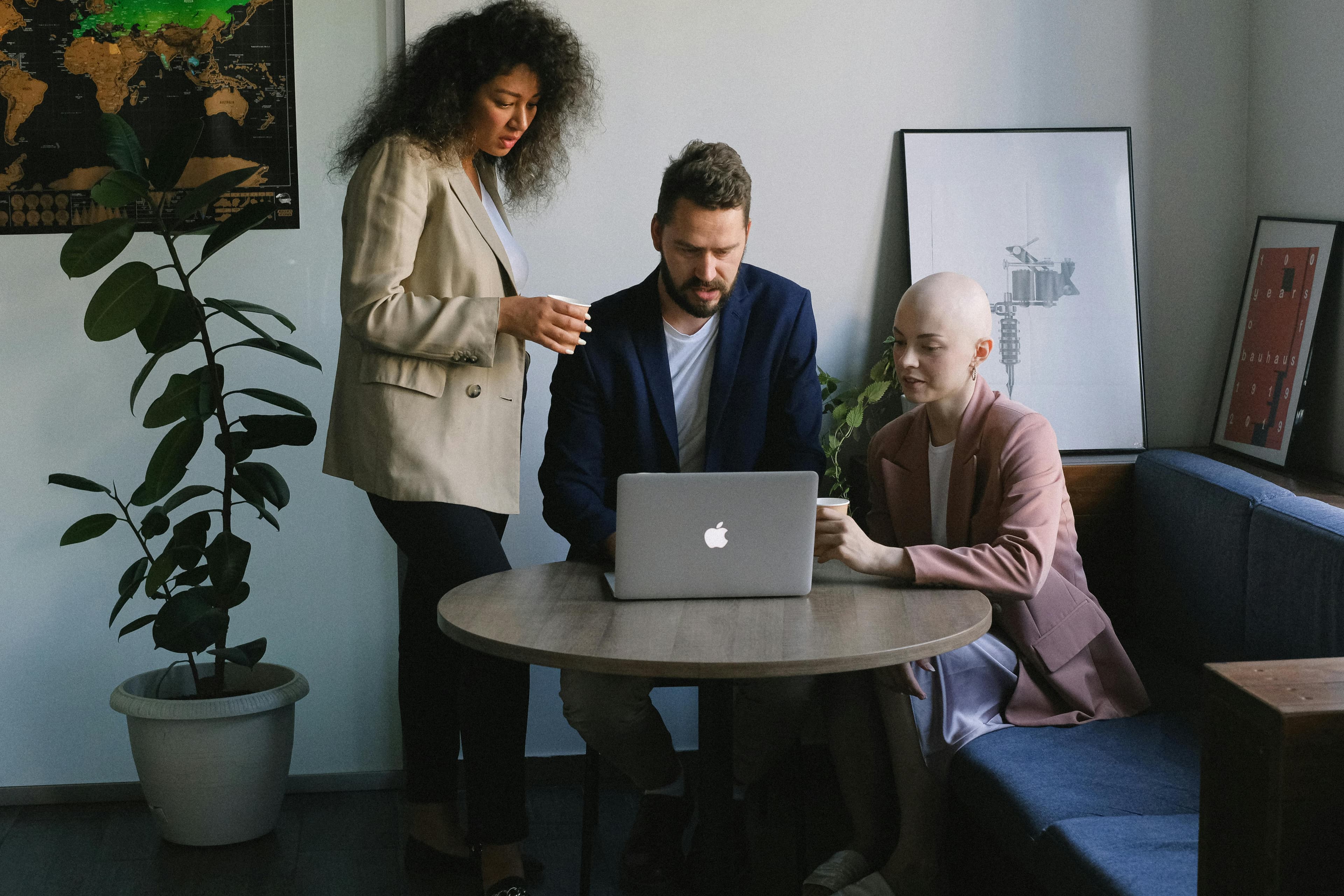 A diverse team of three professionals collaborating around a laptop in a modern office, representing a creative promotional marketing agency.