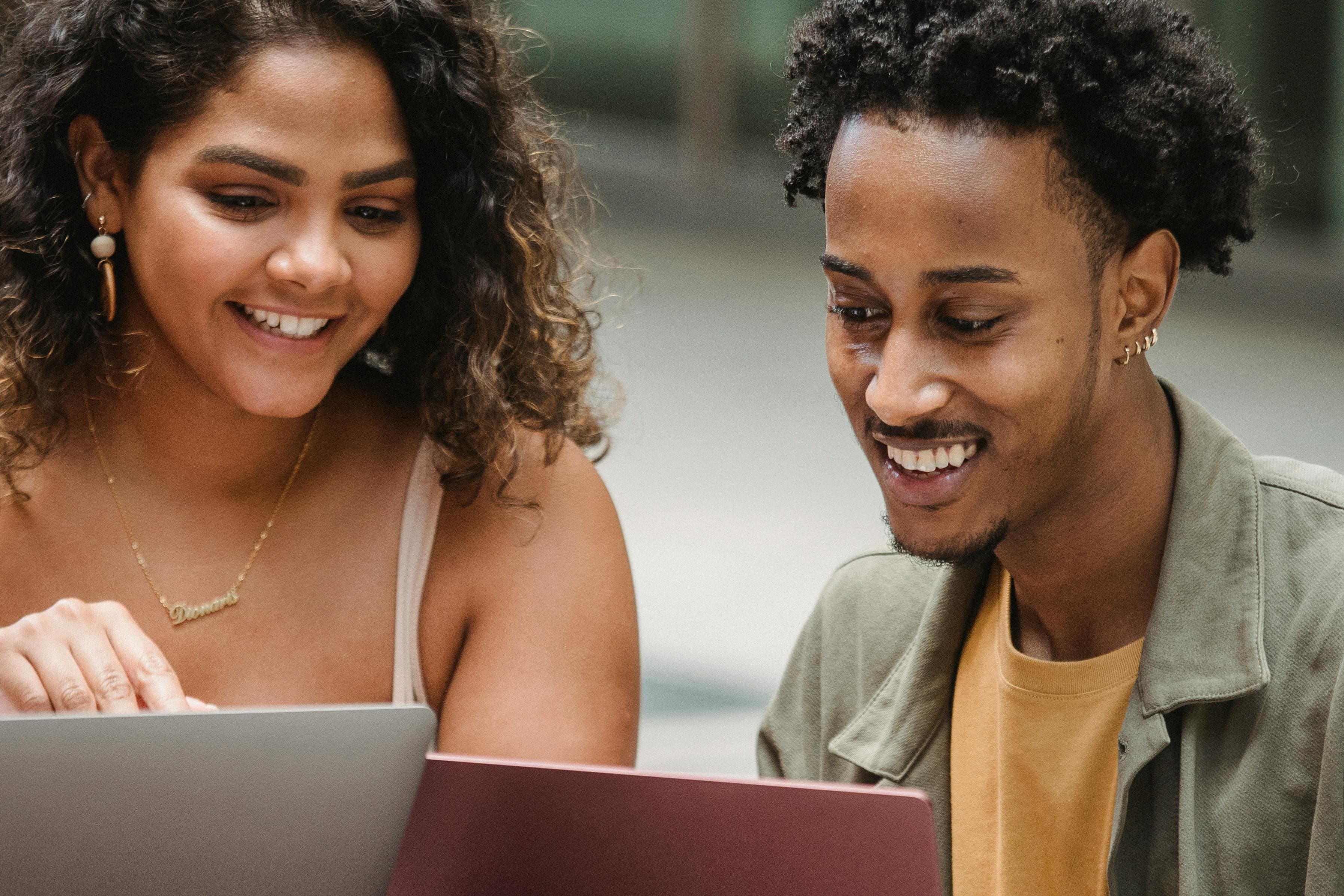 A man and woman smiling and collaborating on laptops, representing the teamwork and collaboration involved in analyzing marketing data analytics to drive business decisions.