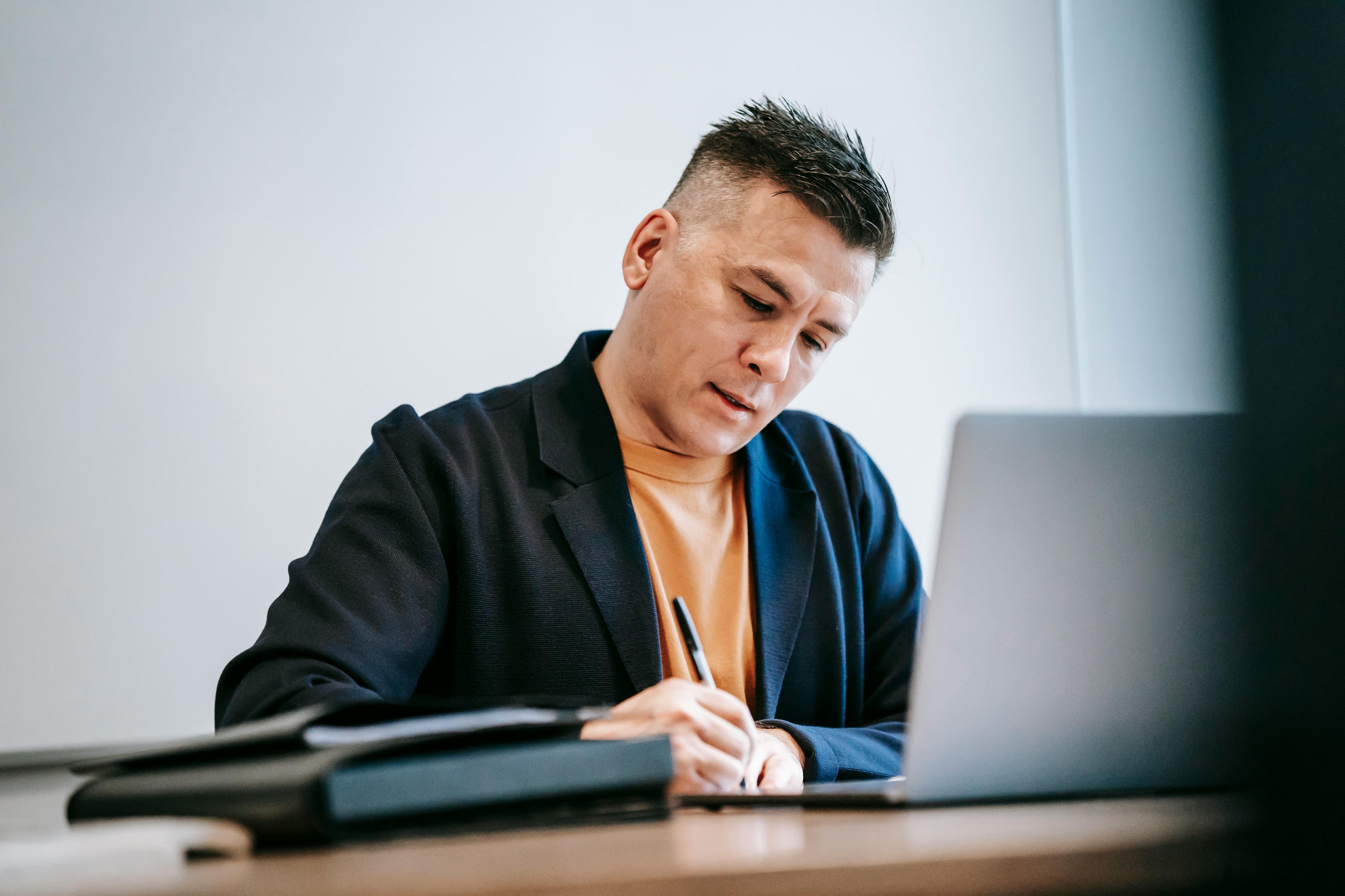 Man working on a laptop and taking notes in a notebook, representing discussions about copywriter salary.