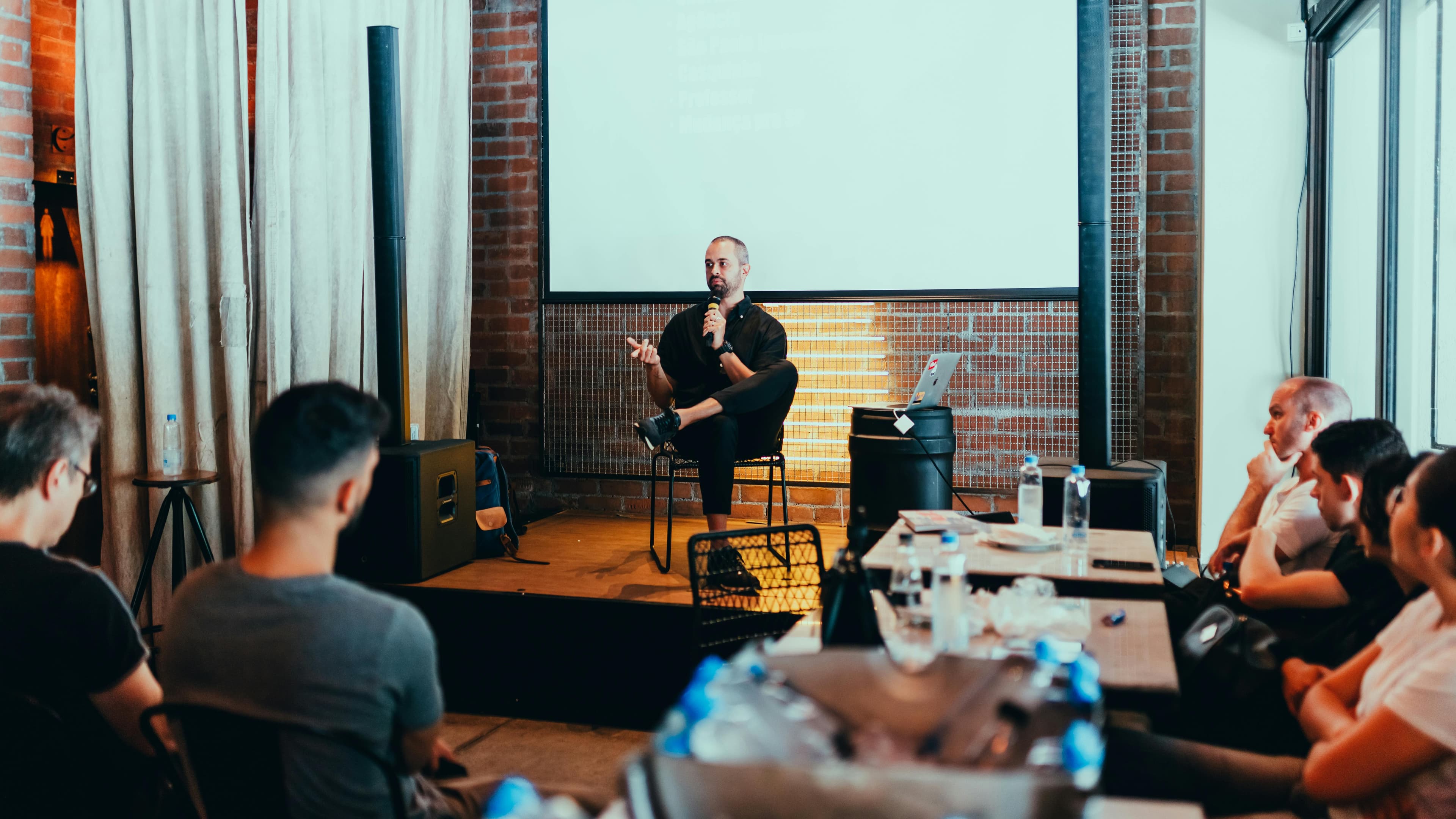 A professional delivering a workshop to a small audience in an industrial-style setting, discussing the benefits and practical applications of a free AI landing page for businesses.