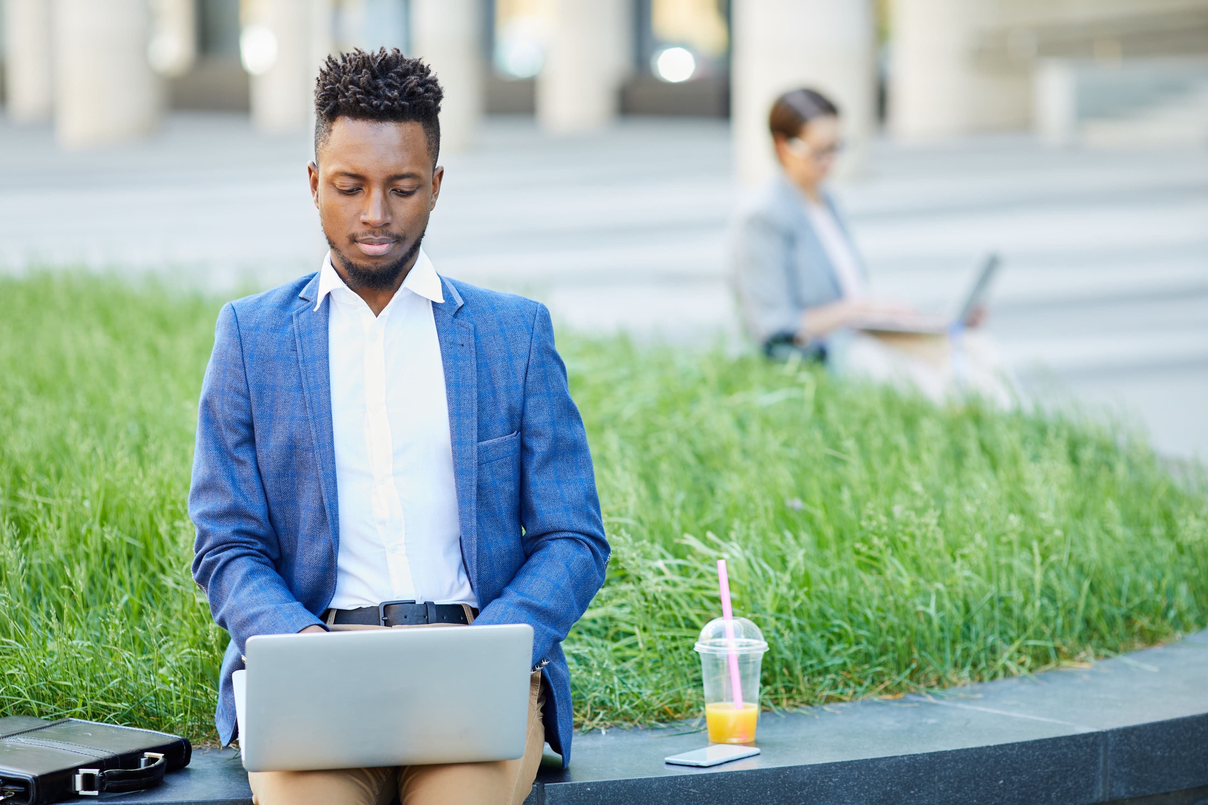 A professional working on a laptop in a vibrant outdoor setting, with a juice cup and a serene backdrop of grass. This image represents productivity and fresh ideas, perfect for inspiring landing pages that highlight modern and adaptable work environments.