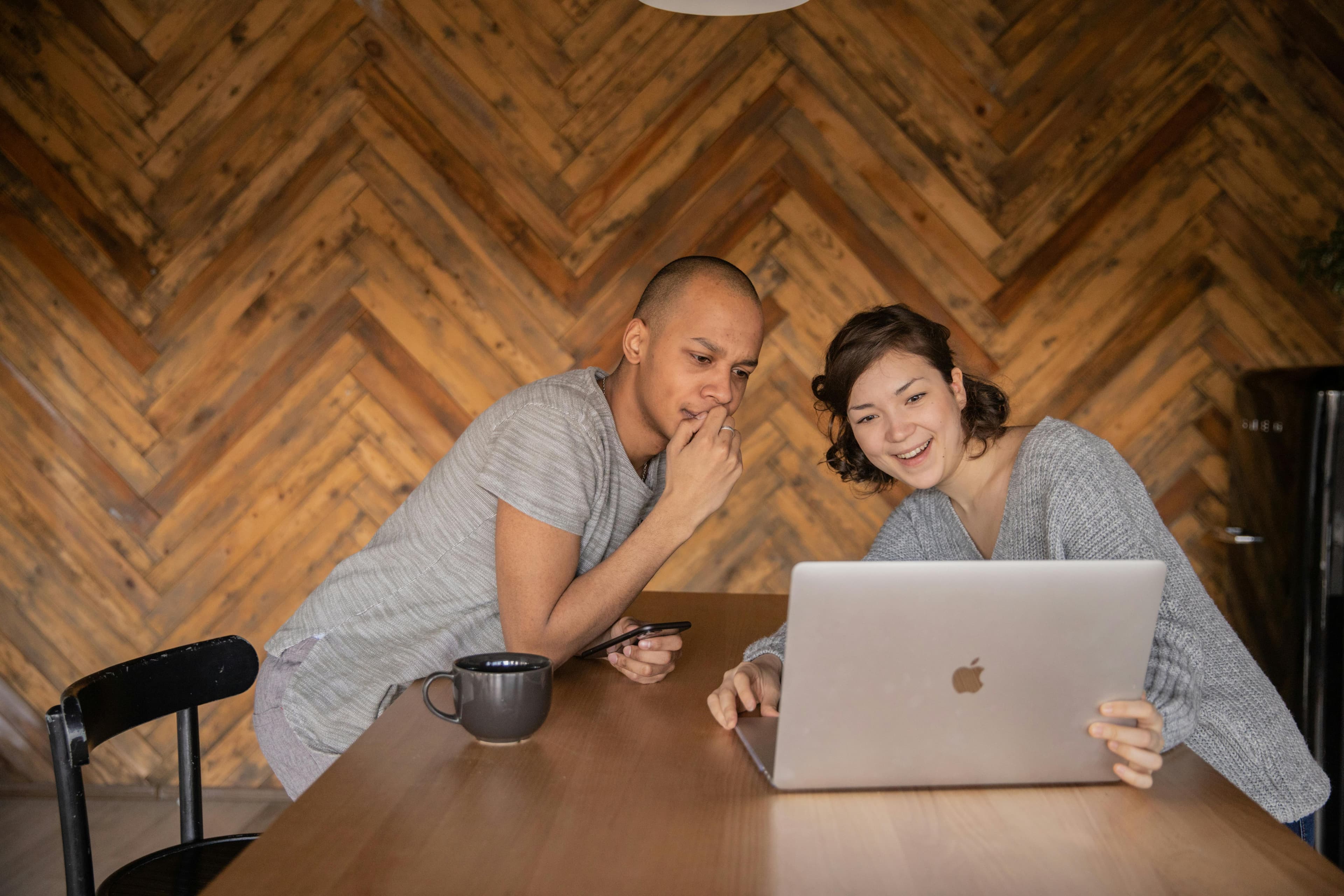 A man and a woman smile as they collaborate on a laptop at a wooden table, embodying teamwork and innovation in "automated content creation."