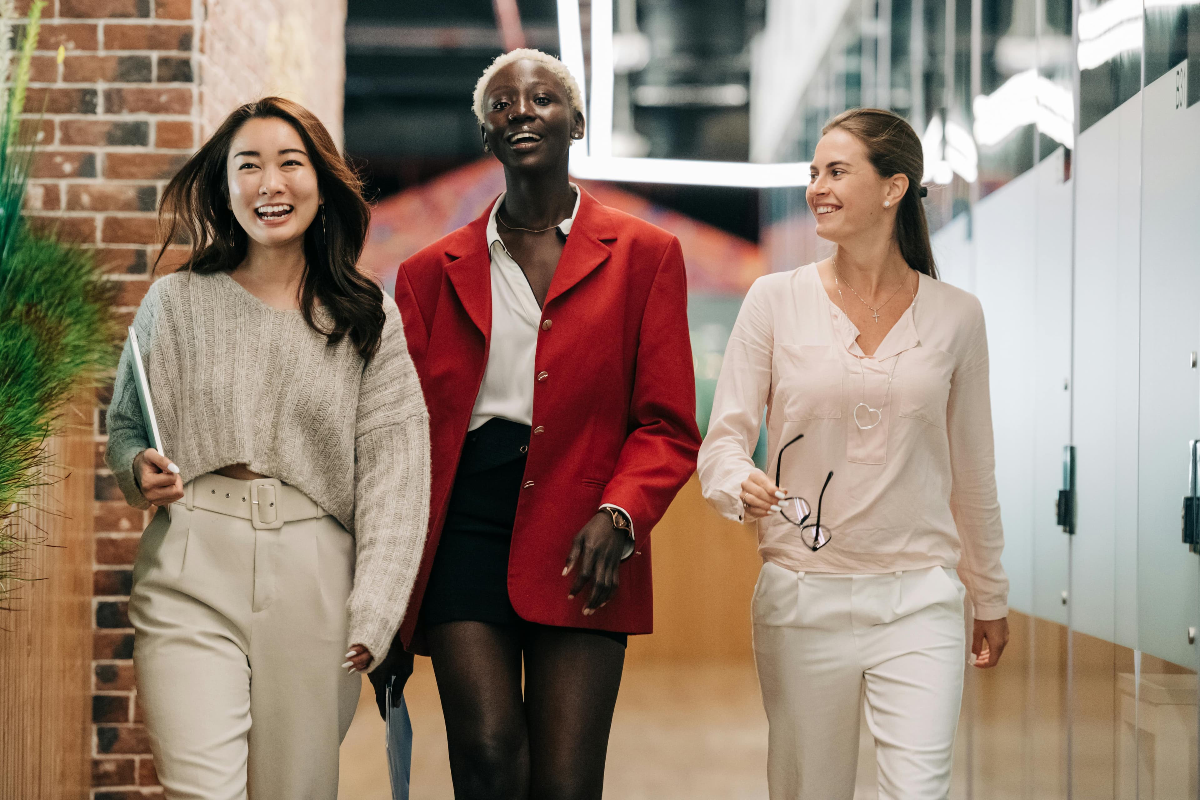 Three professional women walk confidently down a modern hallway, exuding energy and camaraderie. This dynamic shot is ideal for landing page designs promoting empowerment, teamwork, or business innovation.