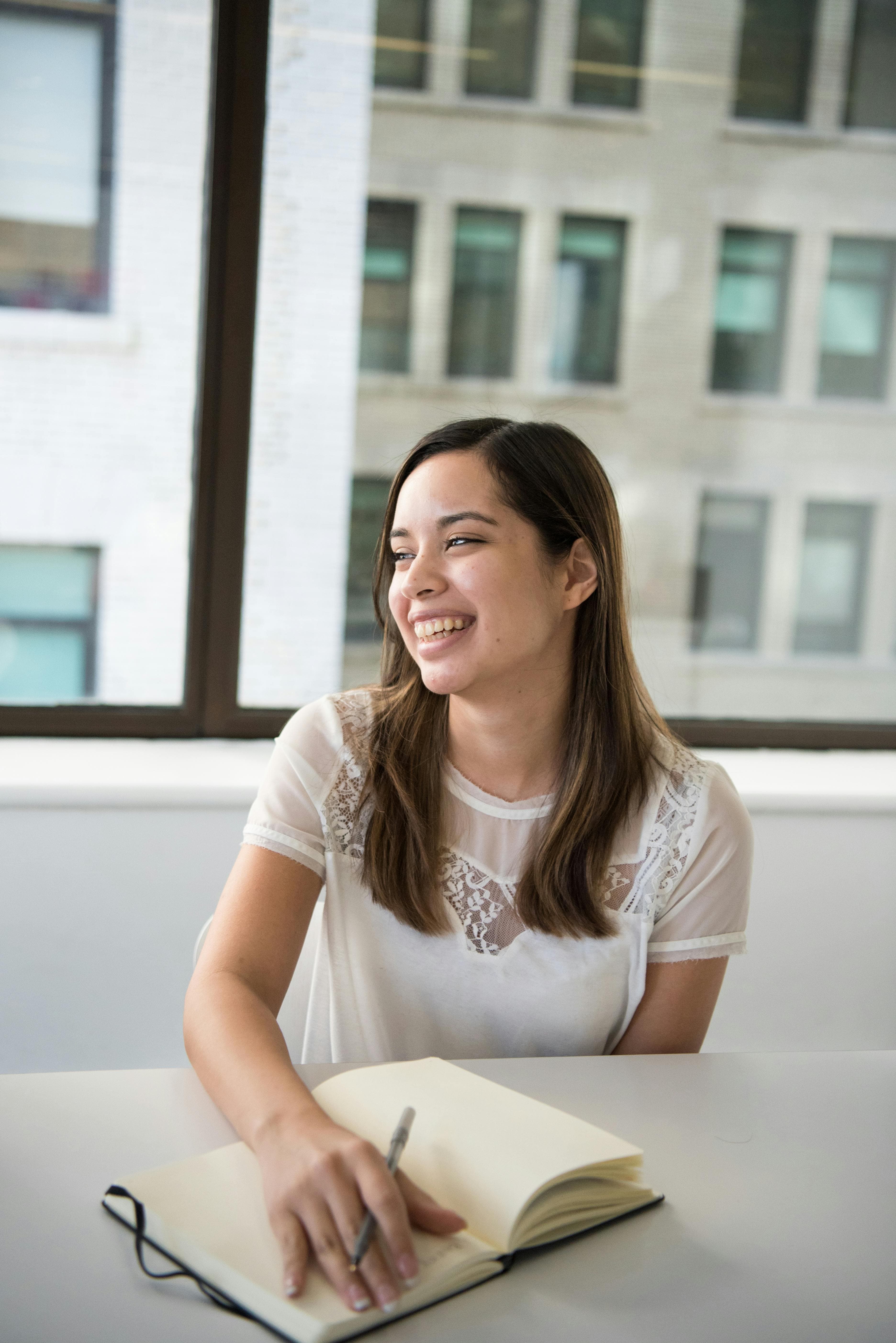 A smiling professional woman writing in a notebook in a well-lit office space, representing creativity and focus for an AI landing page.