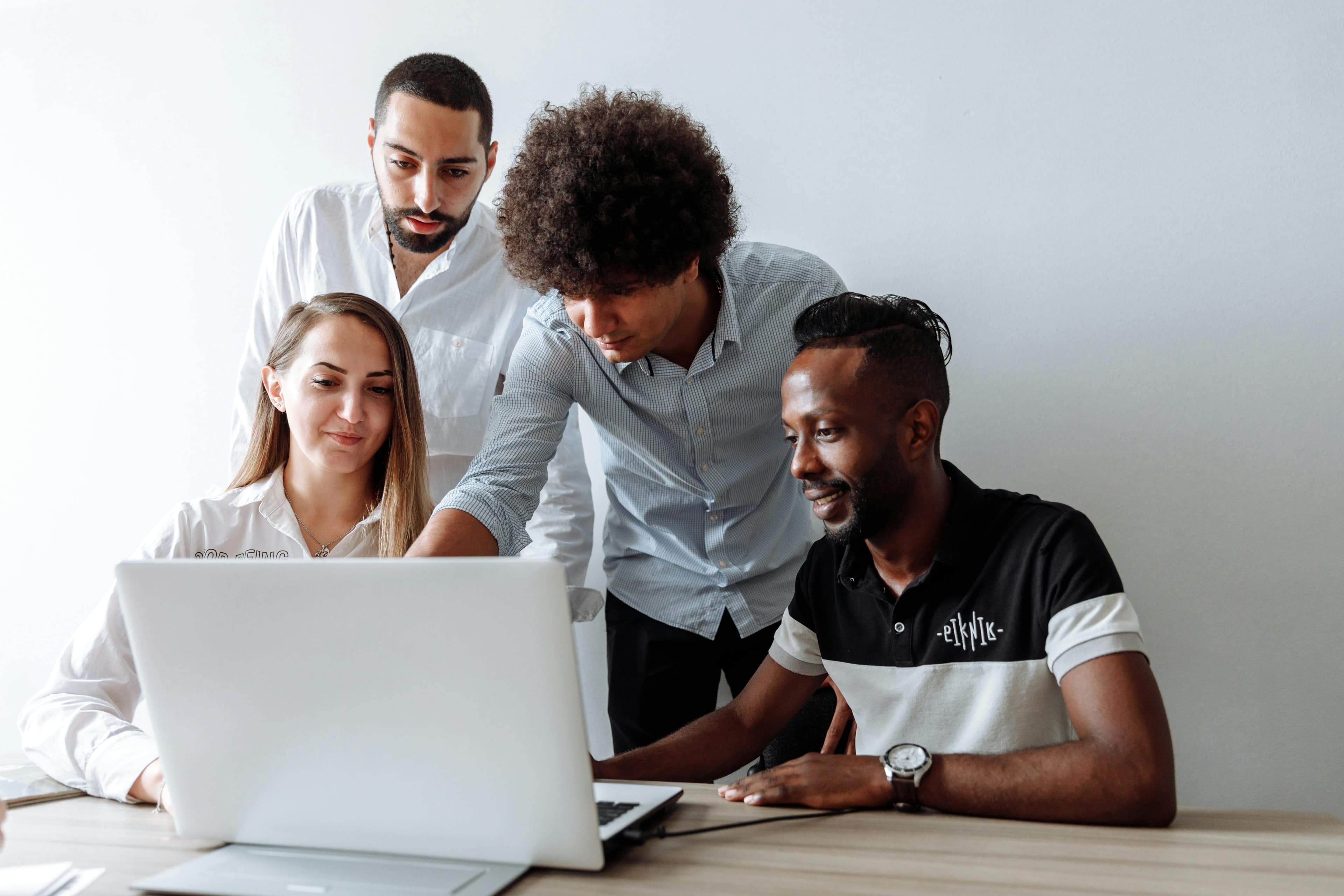 Group of four colleagues collaborating and discussing while looking at a laptop screen, representing copywriter jobs.