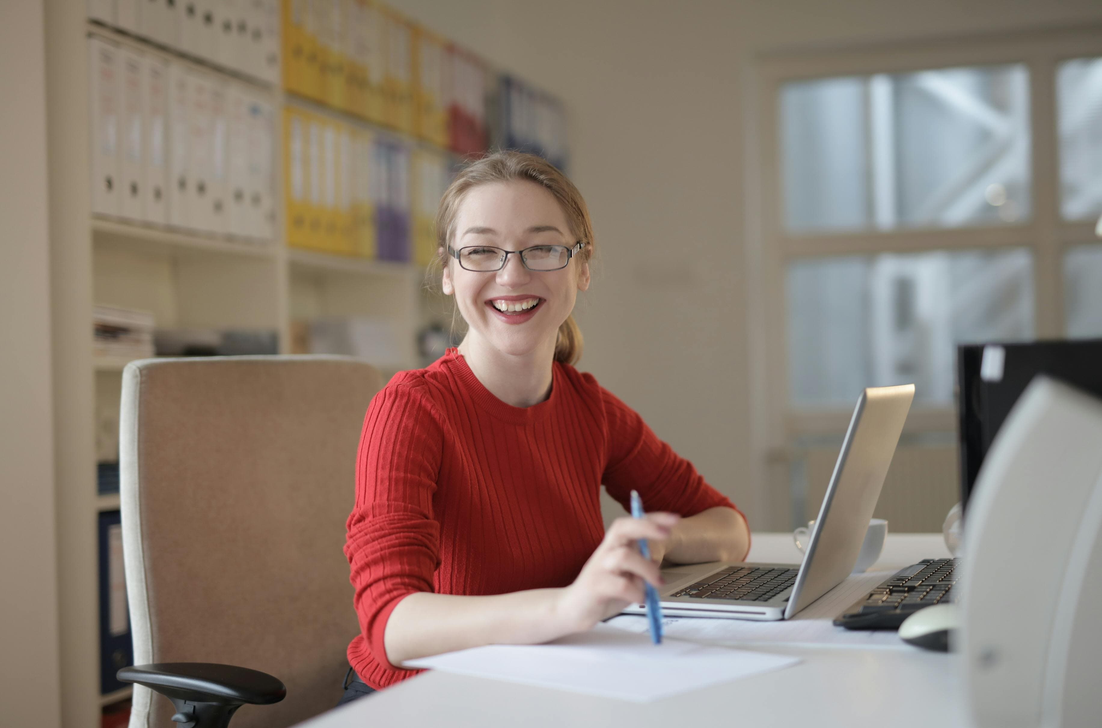 A cheerful woman working at her desk with a laptop and notebook, strategizing product landing page optimization techniques to improve conversion rates.