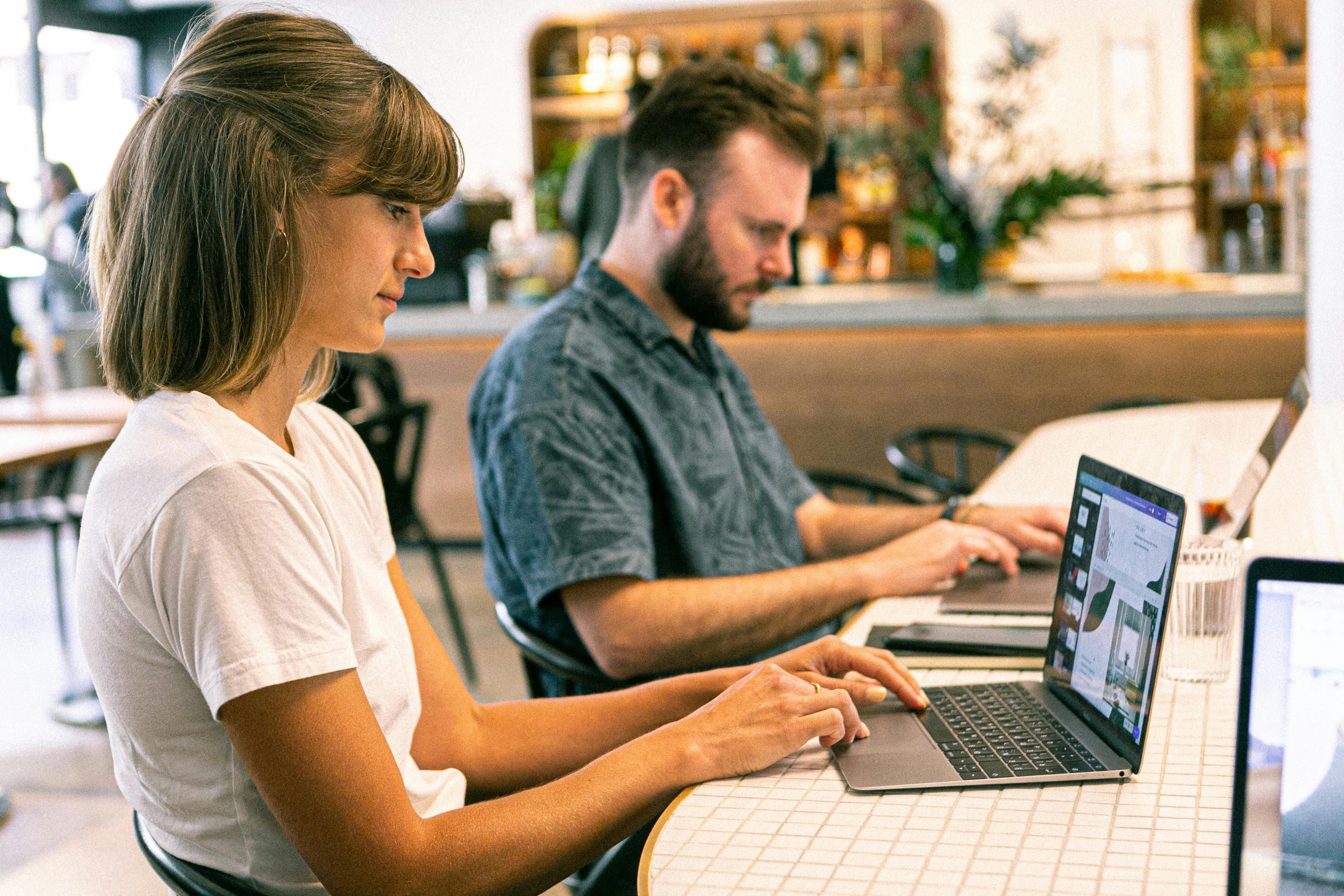 Two professionals working on laptops in a stylish cafe setting, representing a conversion optimization agency.