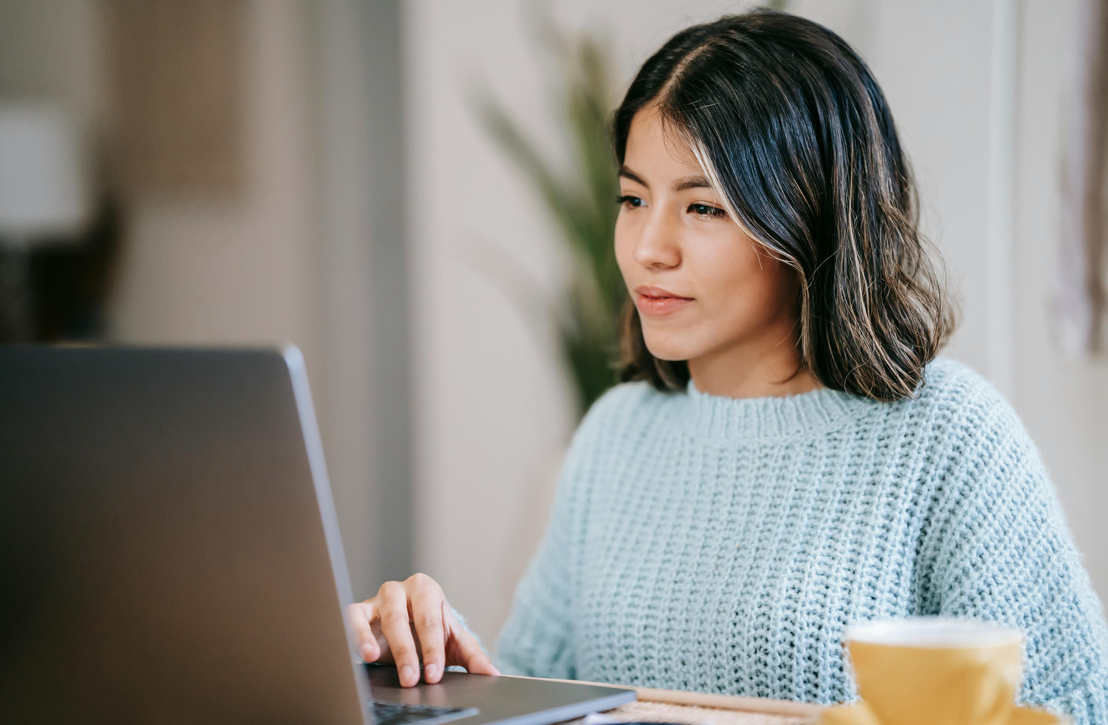 A young woman in a light blue sweater working on a laptop at home, representing digital marketing for small businesses.