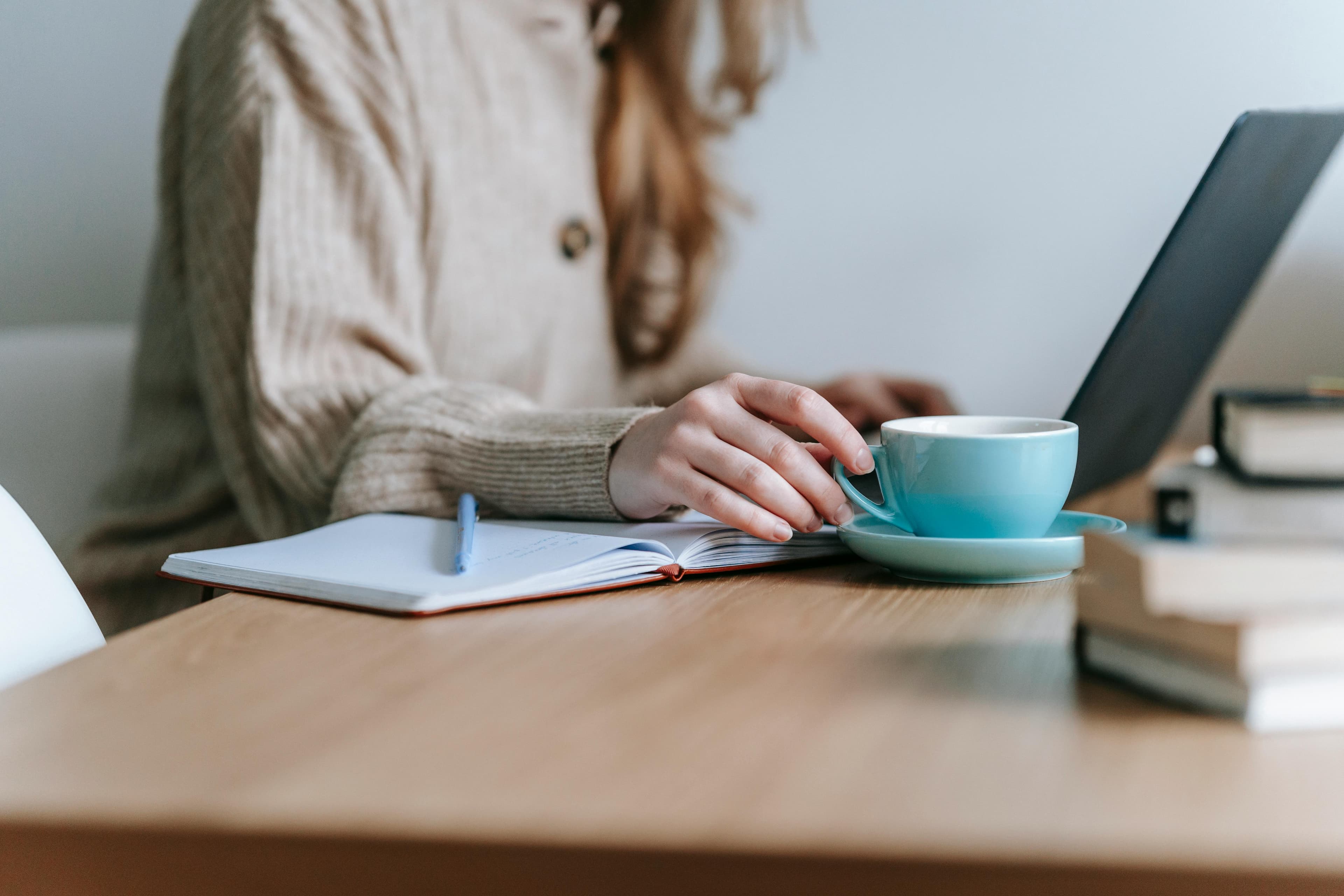 A person working on a laptop with a cup of coffee and an open notebook on the desk, representing a DTC marketing agency.