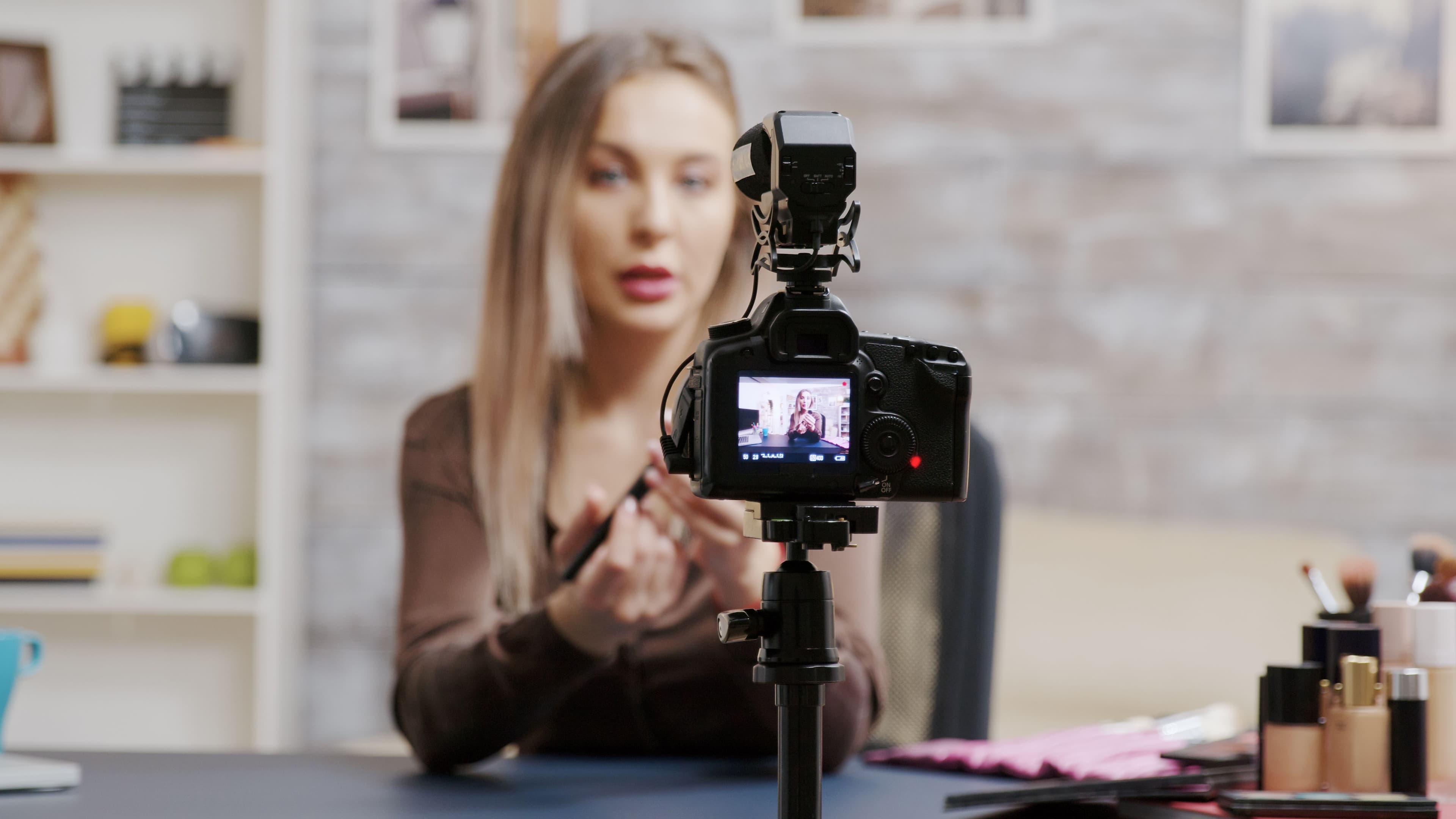 A beauty vlogger recording a video using a professional camera setup, surrounded by makeup products in a well-lit space. This image perfectly illustrates a live stream setting for promoting a product on a landing page.