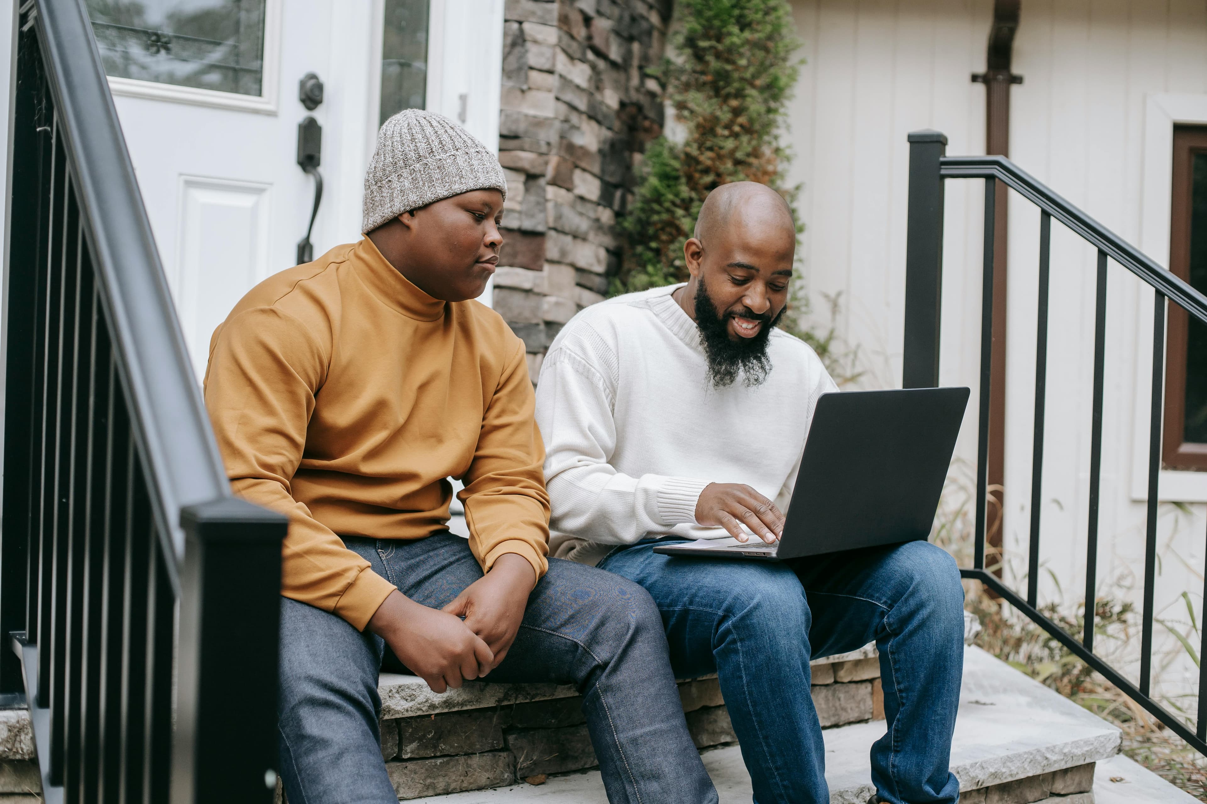 Two men sitting on the steps of a home, working together on a laptop to explore effective techniques for "how to design a website that converts" with practical and user-focused designs.