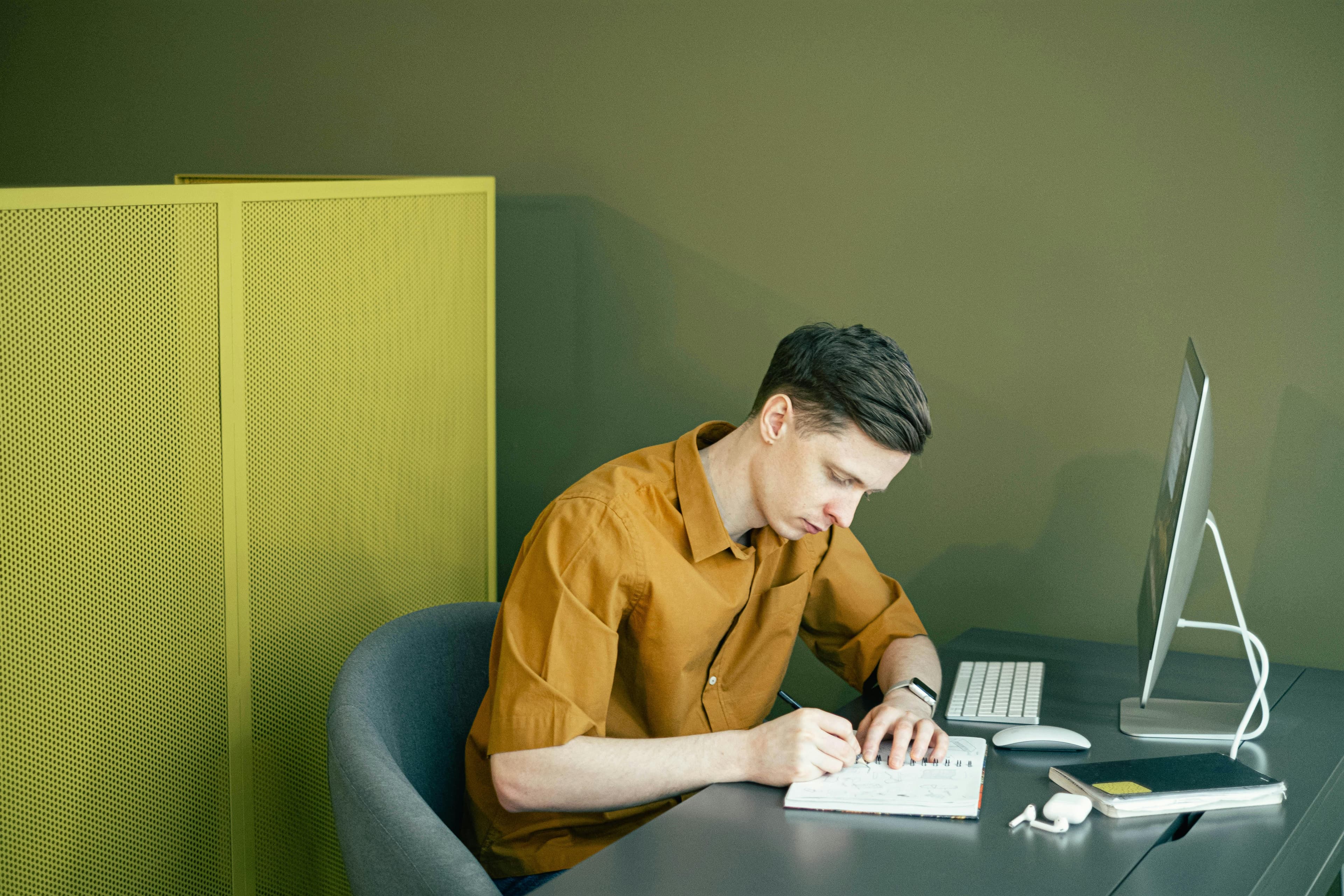 A professional seated at a modern desk, writing in a planner next to a sleek computer setup. An ideal depiction of the meticulous planning involved in designing best lead generation landing pages.