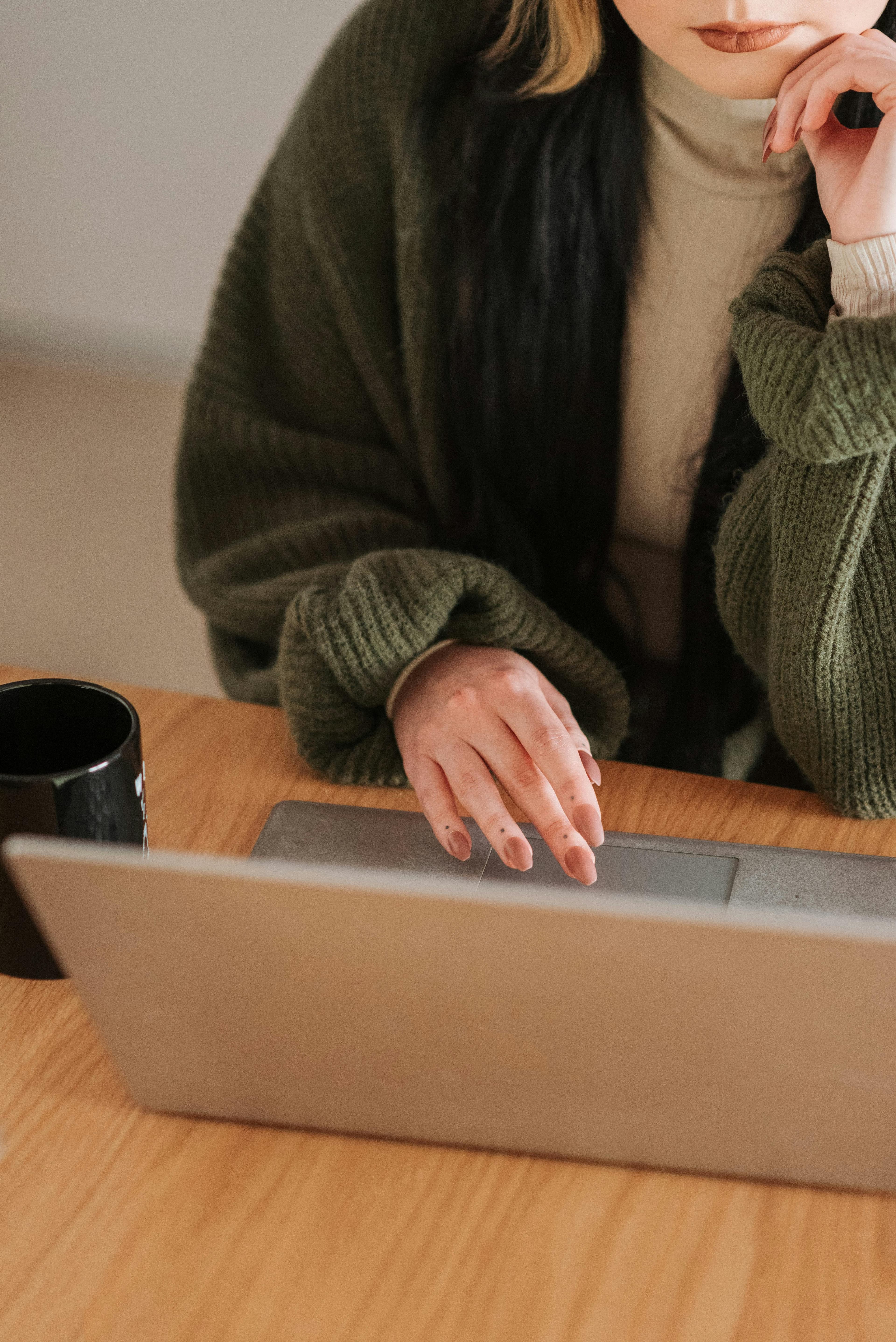  A close-up of a woman’s hands typing on a laptop, with a mug nearby, on a wooden table. This cozy image symbolizes the personal touch and functionality that can be achieved without exceeding a landing page cost budget.