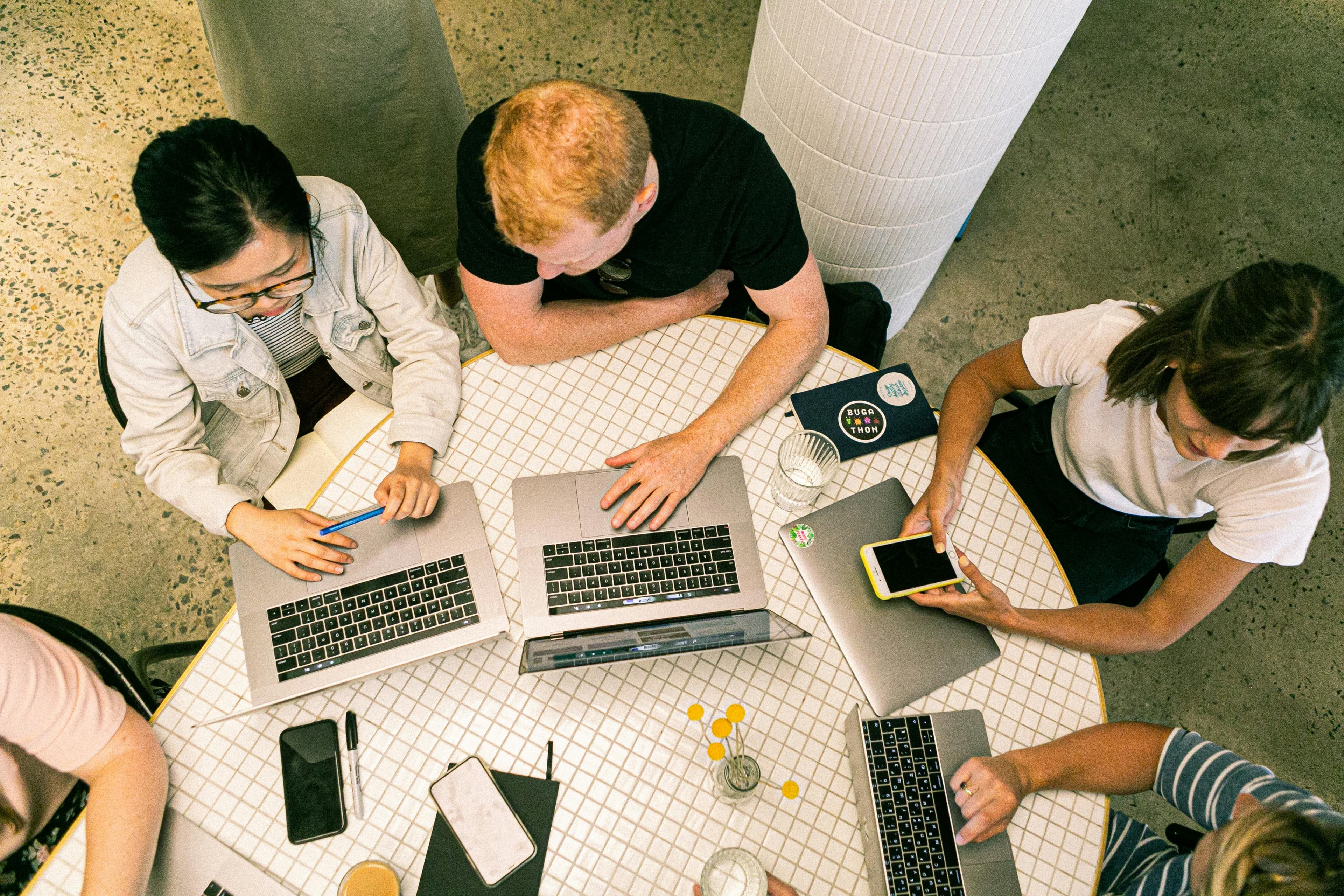 A group of colleagues collaborating around a round table with laptops and smartphones, demonstrating "7 principles of design," including emphasis, harmony, and rhythm in their teamwork setup.