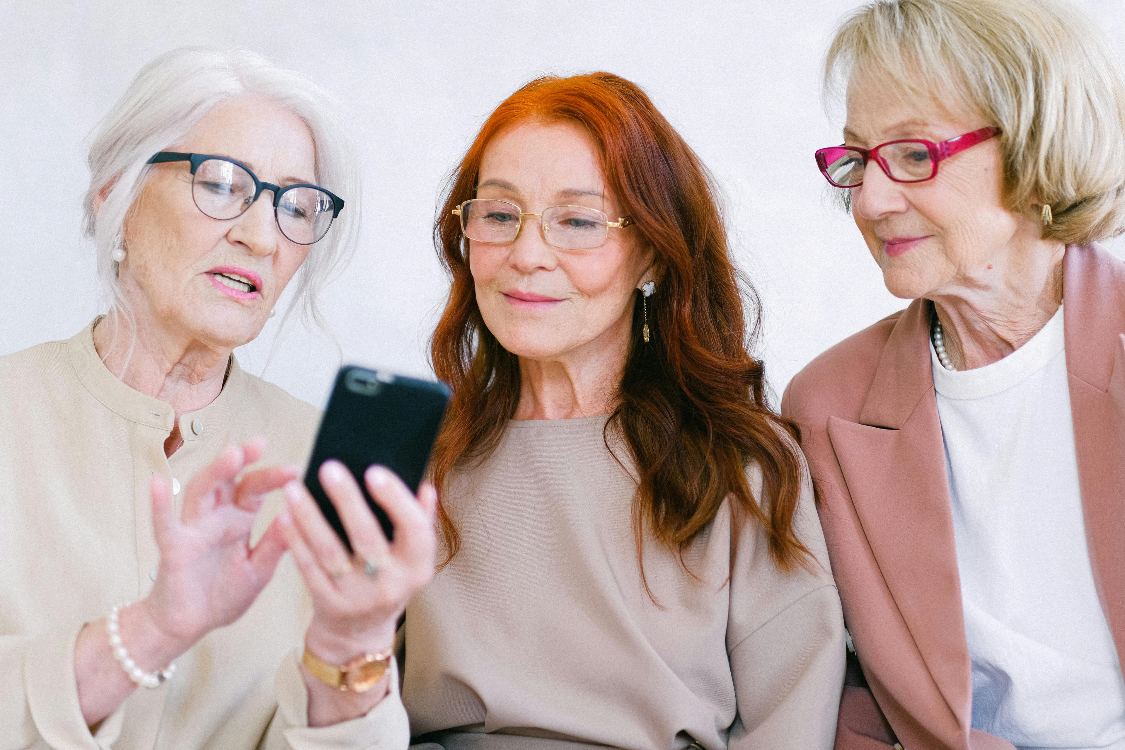 Three senior women gathered together, looking at a smartphone screen, symbolizing the importance of easy-to-navigate and accessible websites that convert across various age groups.