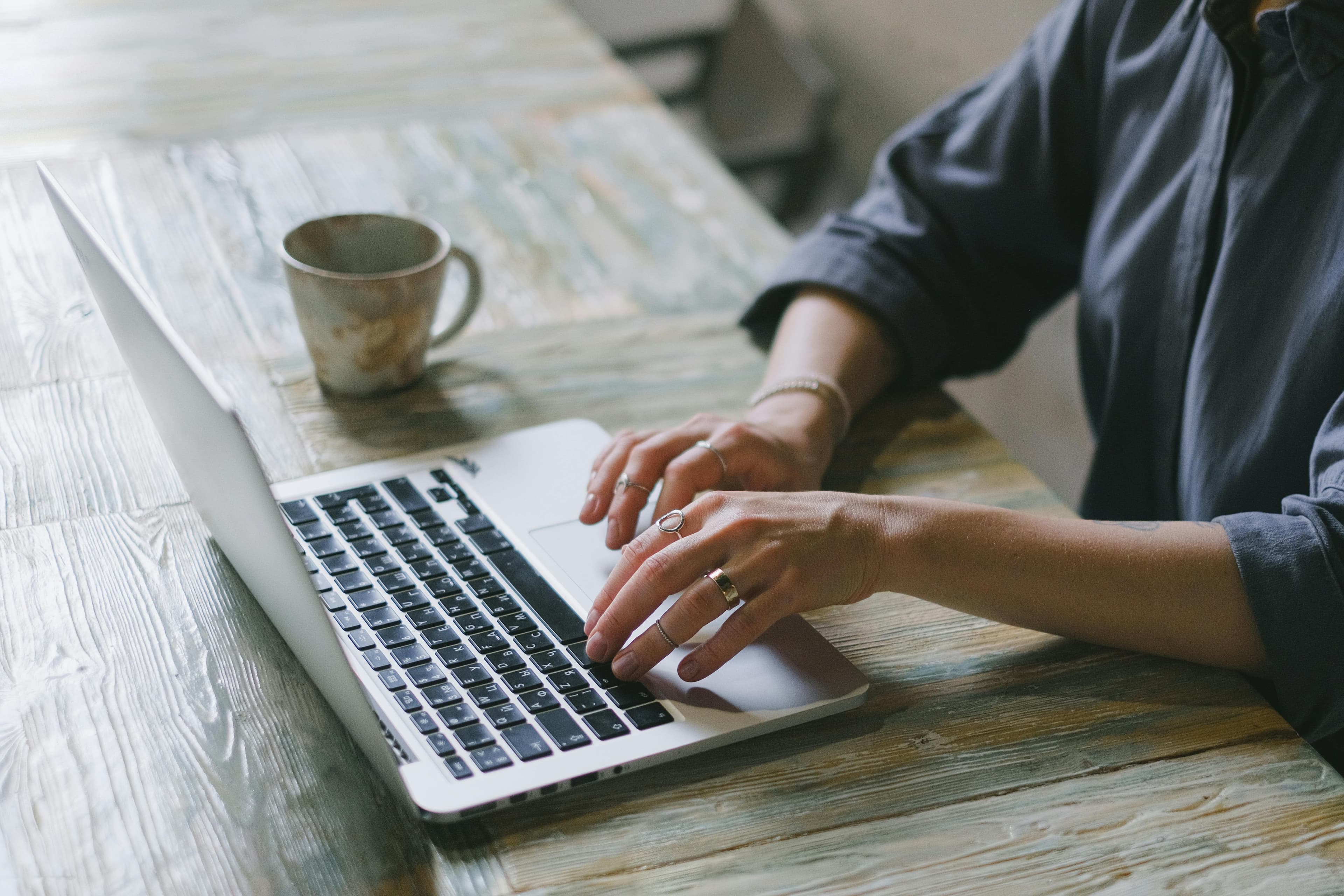 A person typing on a laptop at a wooden table with a coffee mug beside them, representing the focused efforts in achieving marketing conversion.