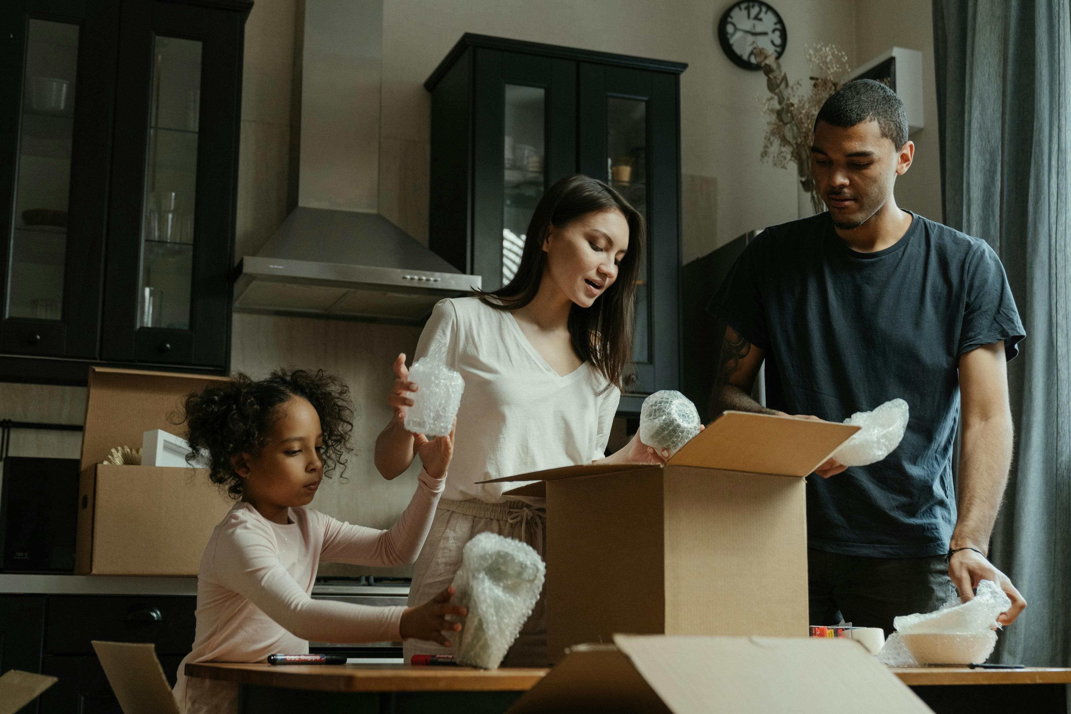 A diverse family collaborates in a modern kitchen, packing items into boxes with bubble wrap, an ideal visual for an affiliate landing page about family collaboration and home organization.