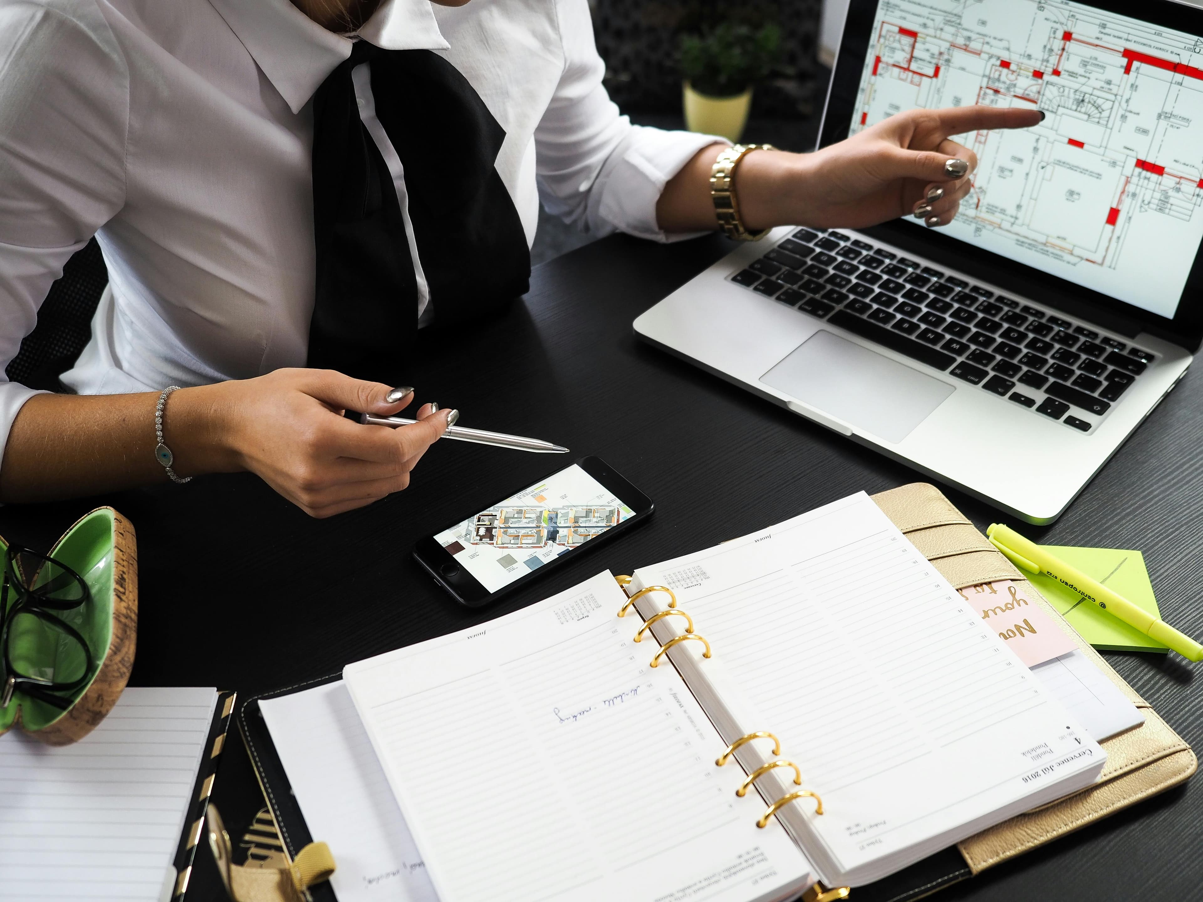 A businesswoman analyzing blueprints and data on a laptop and smartphone, emphasizing detail-oriented planning in a "B2B customer acquisition strategy."