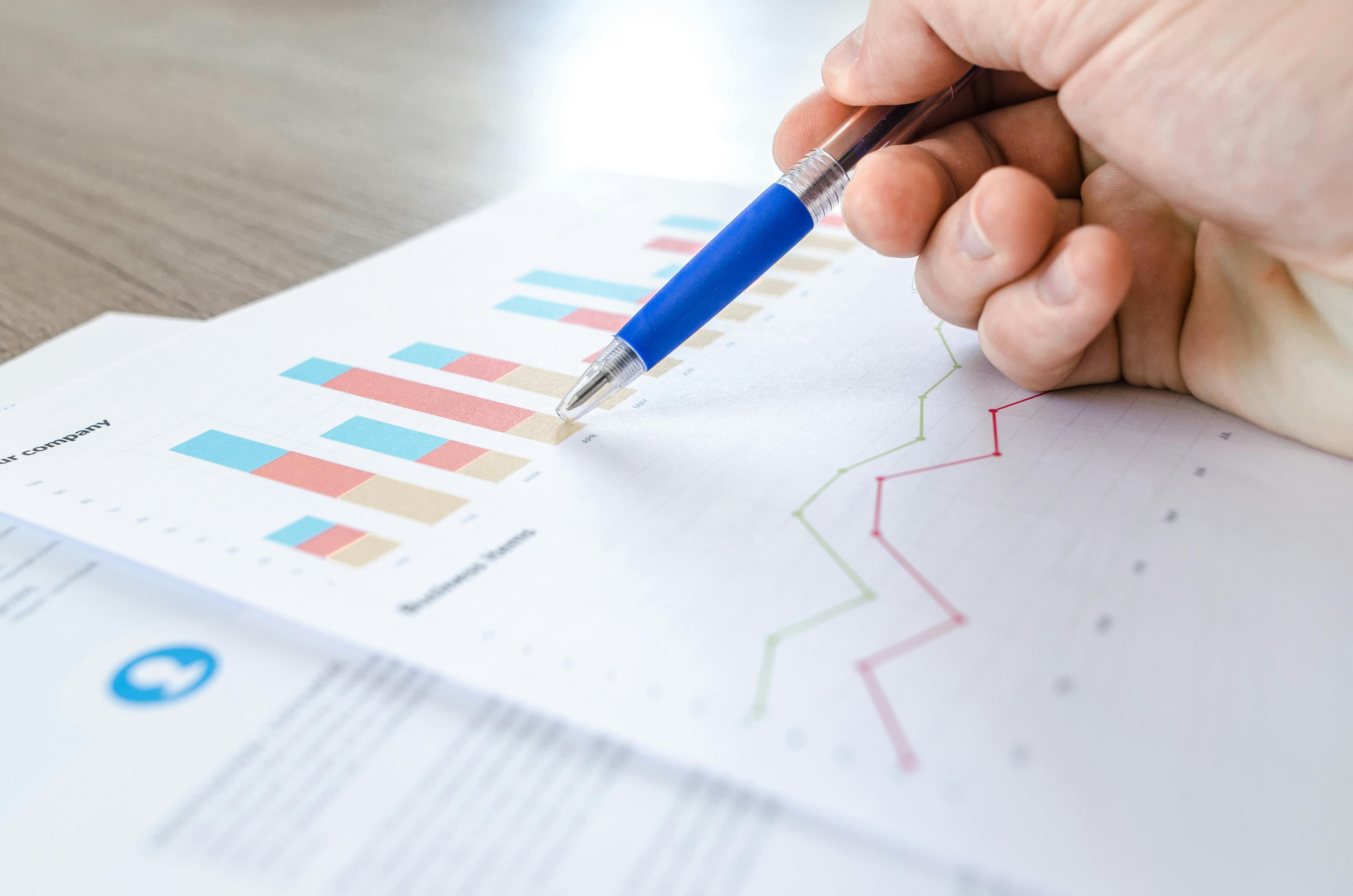 A close-up of a hand holding a pen, analyzing vibrant bar charts and graphs on printed reports—symbolizing data-driven decisions using the best keyword research tools for optimization.