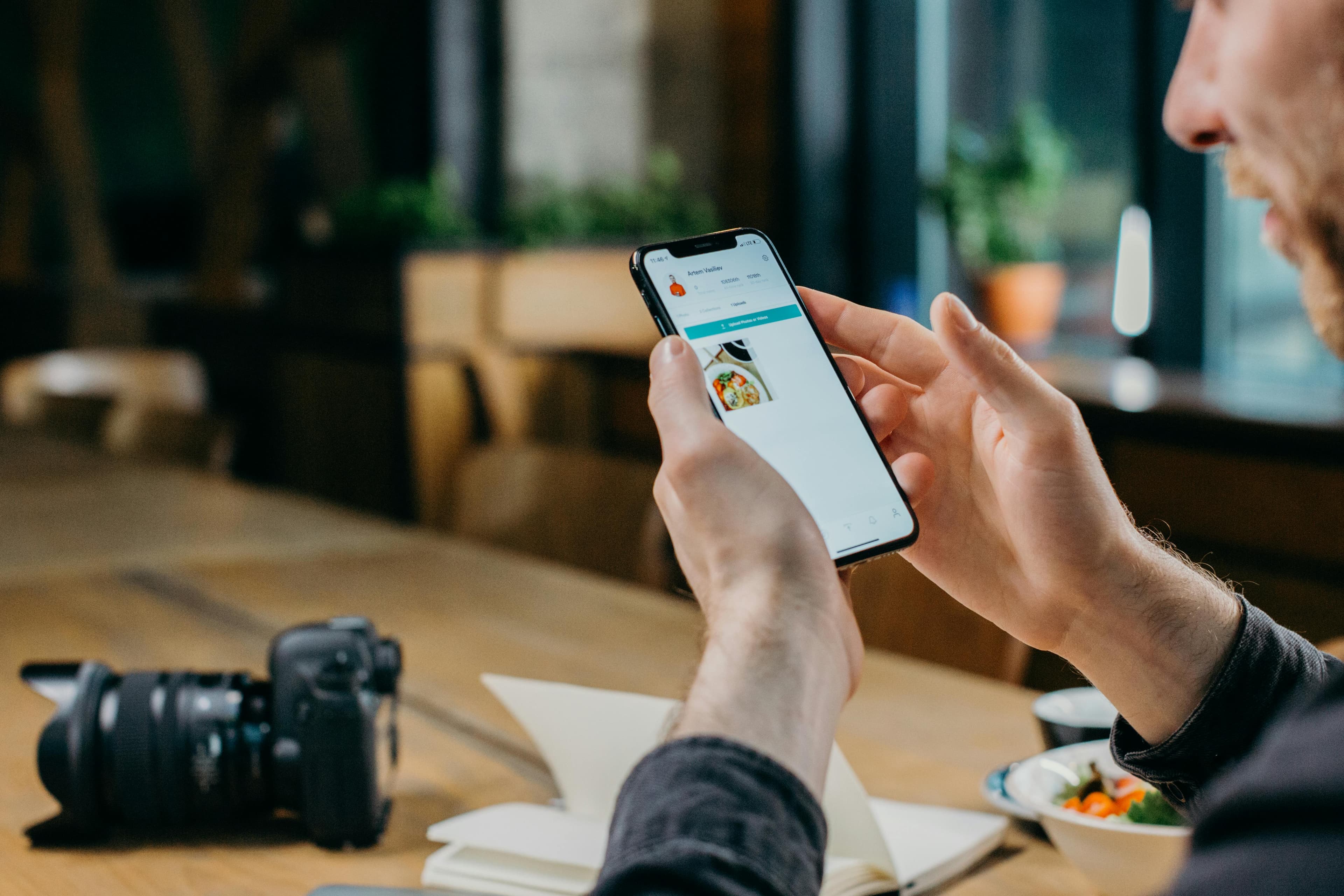  A man sitting at a table holding a smartphone displaying a vibrant product image, depicting the seamless integration of AI-generated ad creatives into marketing strategies.