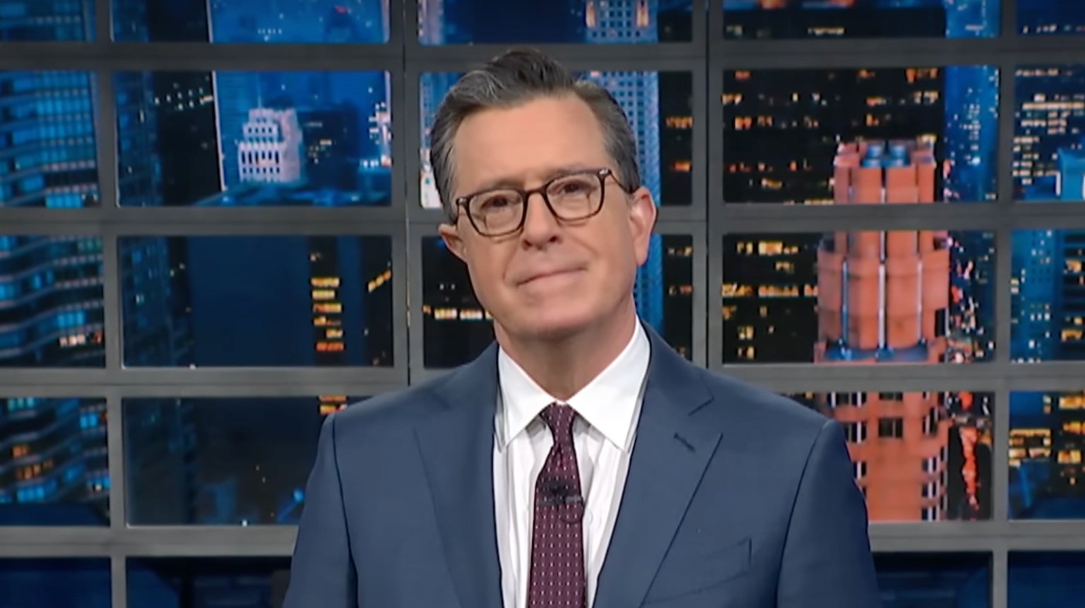 A man in a suit stands on a talk show stage.