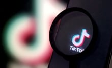 A magnifying glass magnifies a TikTok logo on a phone screen.