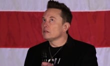 Elon Musk stares upwards in front of a US flag. 