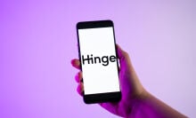 A person holding a mobile phone with the Hinge dating app logo on its screen.