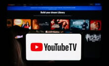 the youtube tv logo on a smartphone in front of a tv showing the youtube tv homepage