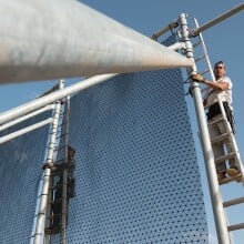 Two men stand on ladders to tend a fog collecting device that resembles a net.