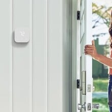 a person leaves through the front door of a home while looking back into the home and smiling. there's an amazon smart thermostat affixed to an interior wall inside the home