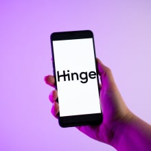 A person is holding a mobile phone with the Hinge logo on its screen