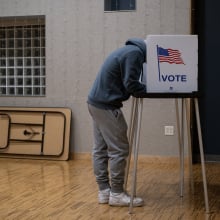 A voter leans over their ballot in a voting booth.