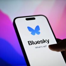 Bluesky app on a smartphone in front of a desktop screen