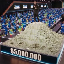 A man stands on a pile of money, surrounded by people in blue tracksuits.