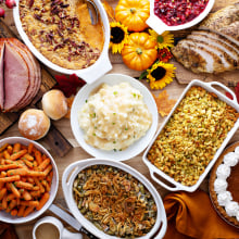 a thanksgiving table spread. there's turkey, ham, mashed potatoes, stuffing. rolls, green bean casserole, cranberry sauce