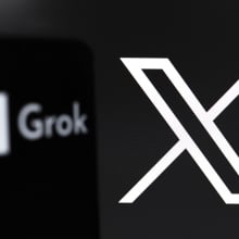 The Grok logo appears on the screen of a smartphone, and in the background, the logo of the social network X (formerly Twitter) is on the computer screen, in Reno, United States, on November 12, 2024. Grok is an artificial intelligence chatbot generative technology developed by xAI, with an initiative from Elon Musk. The company tests a free version of the service that will be available soon.