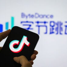 A person holds a smartphone displaying the Douyin logo (the Chinese version of TikTok), with the ByteDance company logo in the background