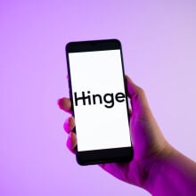 A person holding a mobile phone with the Hinge dating app logo on its screen.