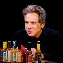 A man sits at a table covered in hot sauce in a dark room.