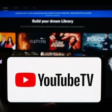 the youtube tv logo on a smartphone in front of a tv showing the youtube tv homepage