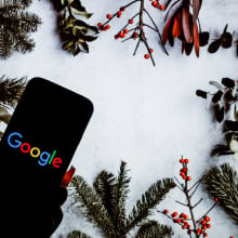 a phone displaying the Google logo surrounded by boughs of holly and such