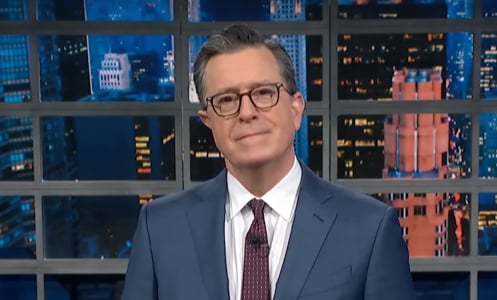 A man in a suit stands on a talk show stage.