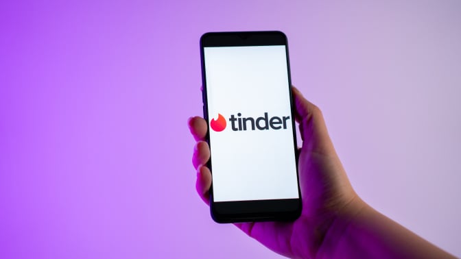 A person is holding a mobile phone with the Tinder dating app logo on its screen